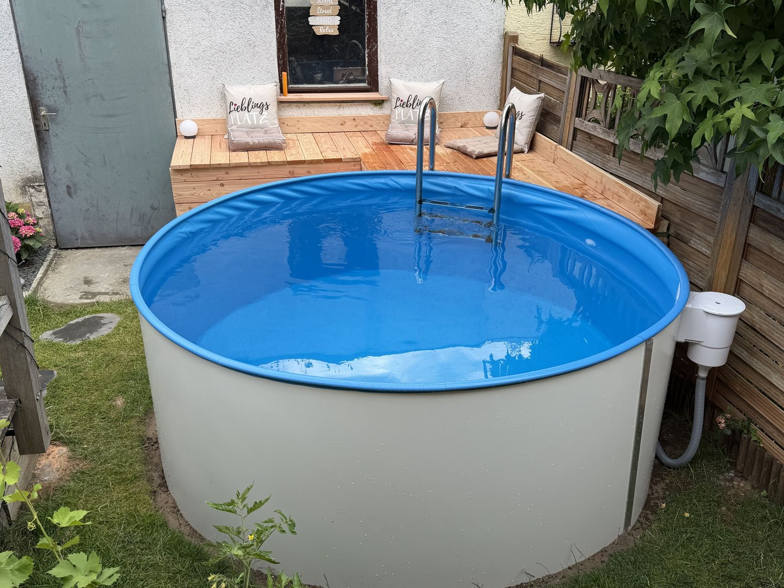 Fertiger Pool mit Edelstahlleiter und Sonnenpodest aus Holz in einem Garten